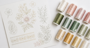 Artistic flat lay of custom embroidery pattern design paper next to spools of embroidery thread