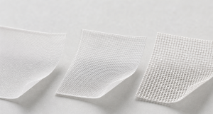 Three square mesh fabric samples arranged in a row showing increasing density from an ultra-fine translucent weave on the left to a coarse open weave on the right, white threads on a light grey studio surface, corners gently curled upward