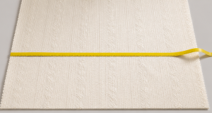 Yellow fabric measuring tape stretched across a broad piece of ivory embroidery fabric showing its industry standard width