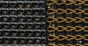 Extreme macro of the reverse side of a sequin fabric divided vertically into two stitching methods: tight interlocking silver lock-stitch cords on the left and looped gold chain-stitch cords on the right, both on a black mesh base under a raking work light