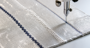 Close-up of lock-stitch and chain-stitch seams sewn on silver sequin fabric with a sewing machine needle working a third seam
