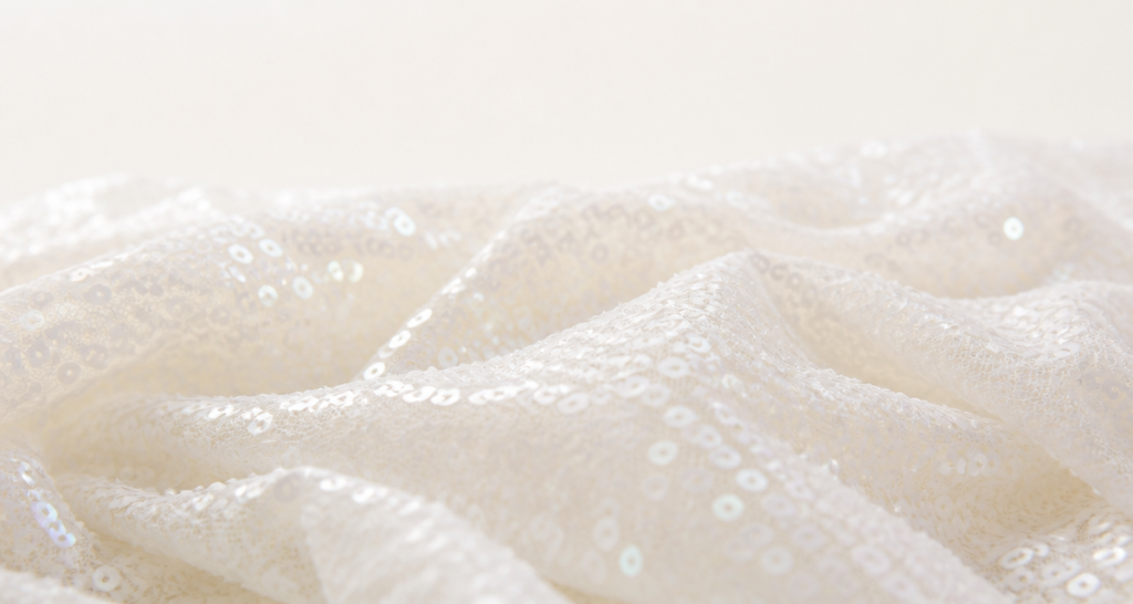 Pearly white shimmering sequins on ivory mesh fabric in soft focus