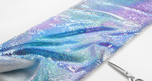 Unfolded length of iridescent sequin fabric laid diagonally with a pair of scissors for wholesale by-the-yard fabric buying